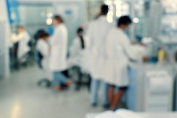 Several people in lab coats work and move around in a laboratory setting, surrounded by scientific equipment and workstations; the image is intentionally blurred.