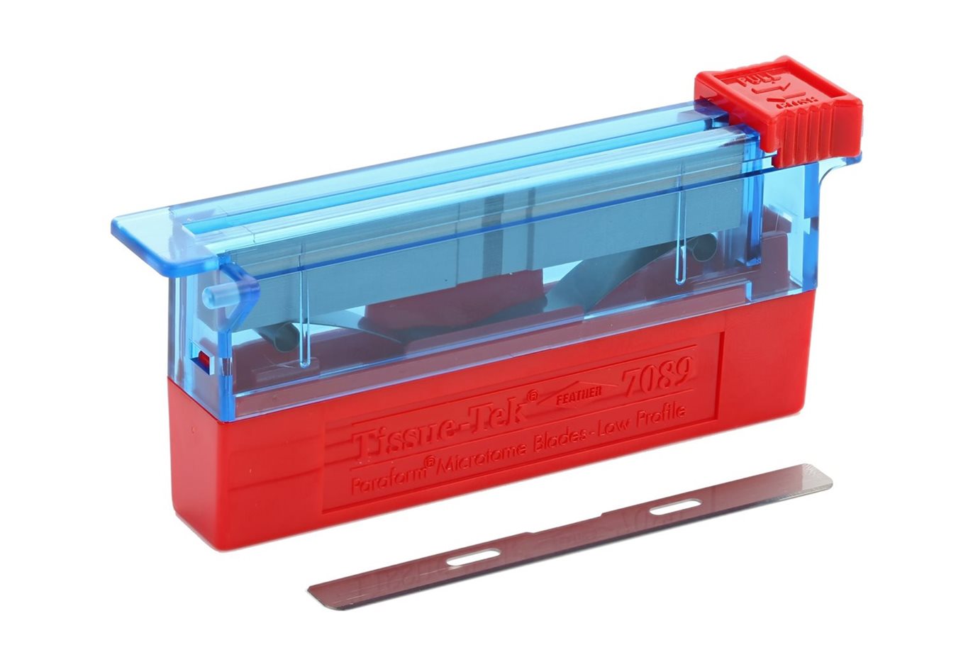 A red and blue plastic tissue block trimmer with a metal blade placed in front of it on a white background.