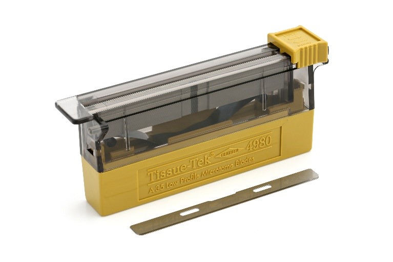 A yellow and clear plastic dispenser labeled "Tissue-Tek 4980" contains microtome blades, with one blade removed and placed in front.