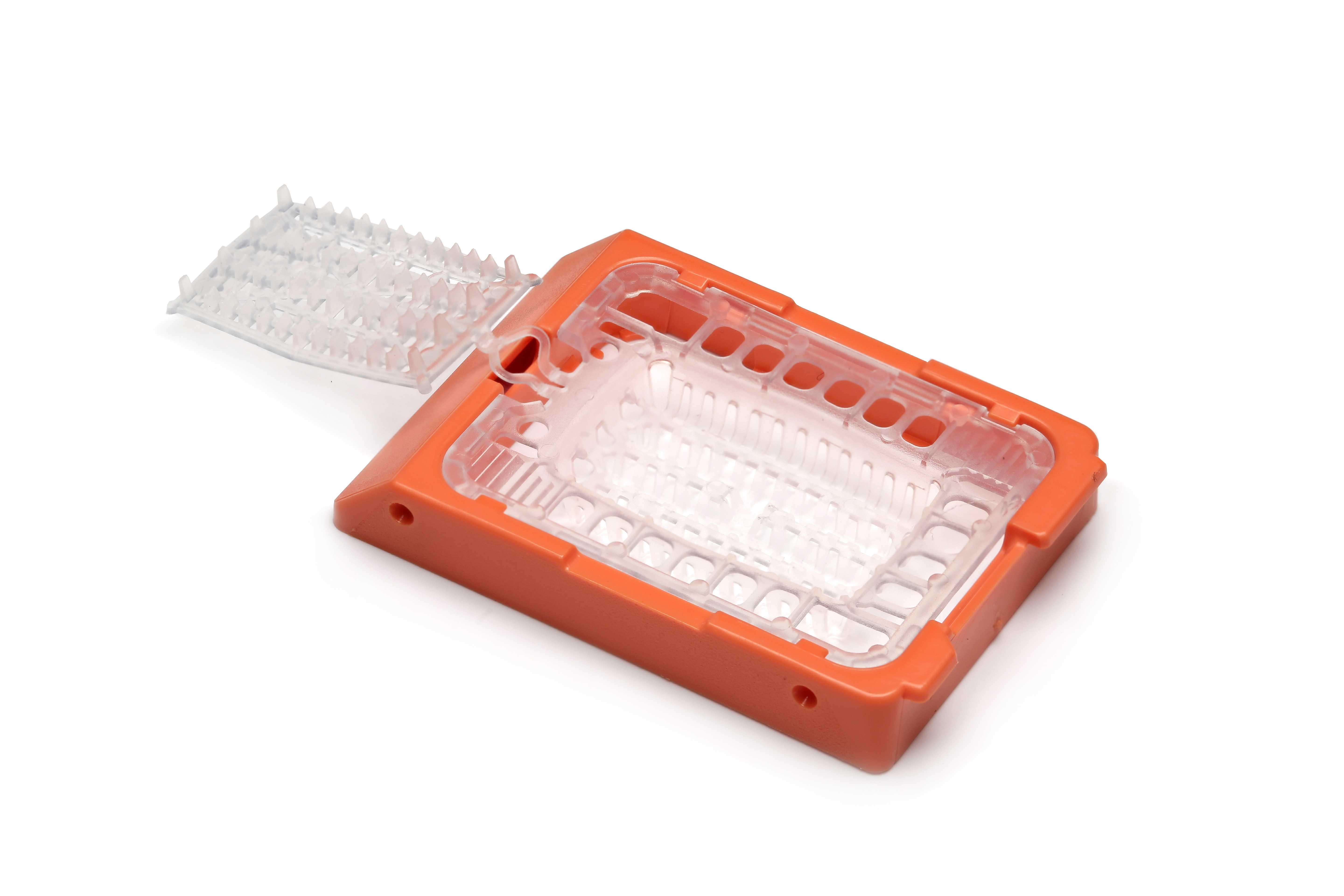 A plastic laboratory tissue cassette with an orange base and a hinged clear lid, used for holding and processing biopsy samples.