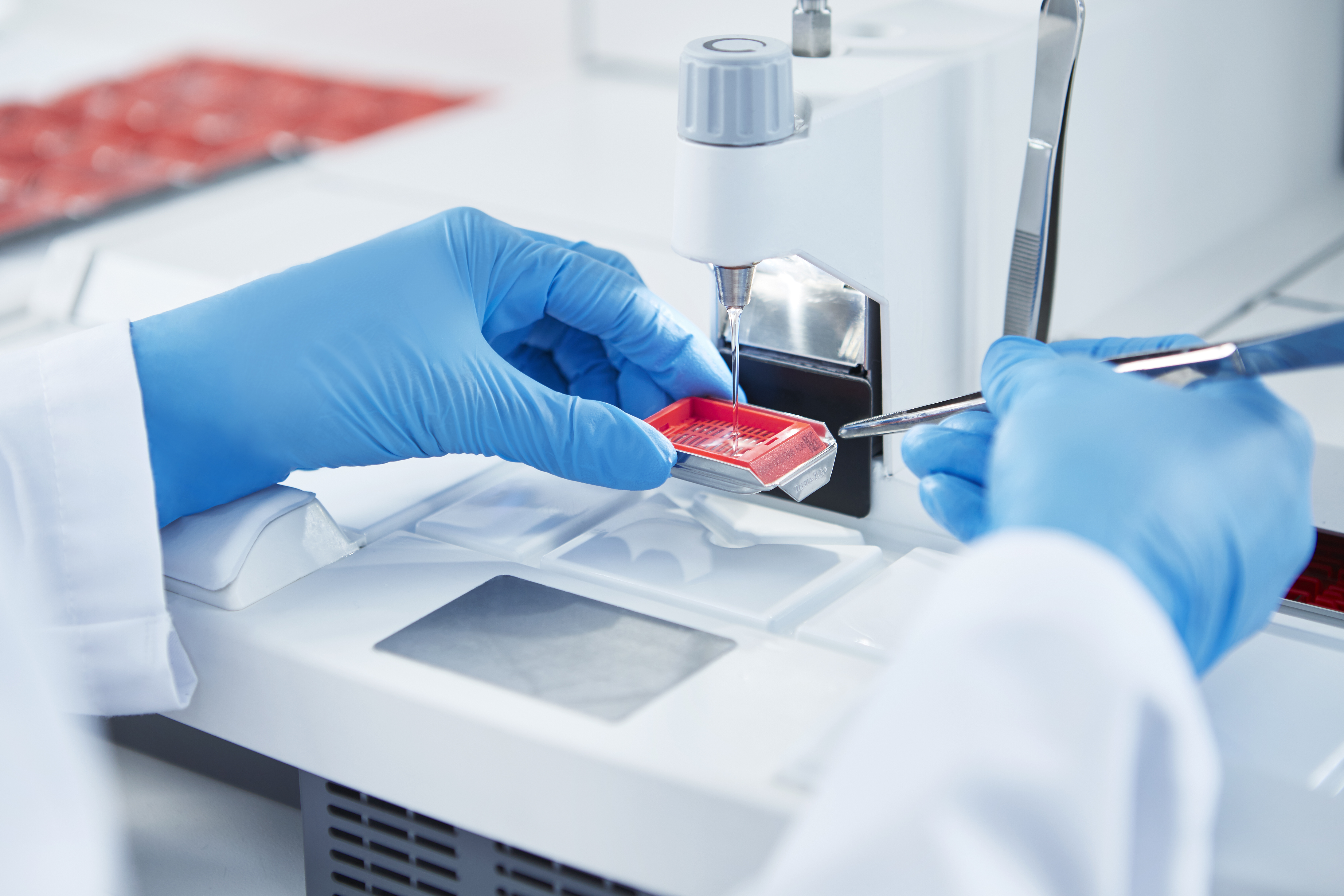 A scientist in blue gloves uses tweezers and lab equipment to prepare a sample slide in a laboratory setting.