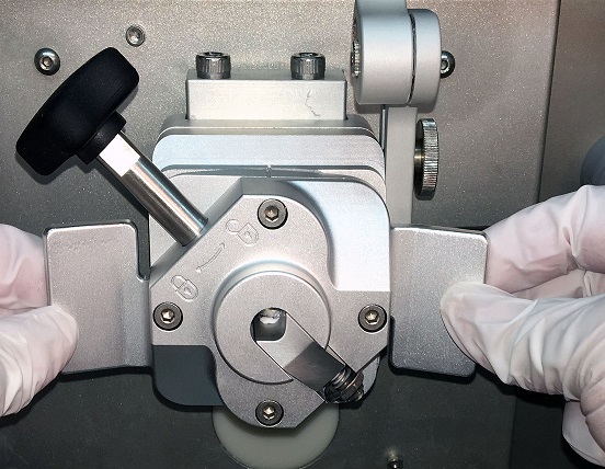 Gloved hands adjusting a microtome machine, used for slicing thin sections of material for microscopic examination.