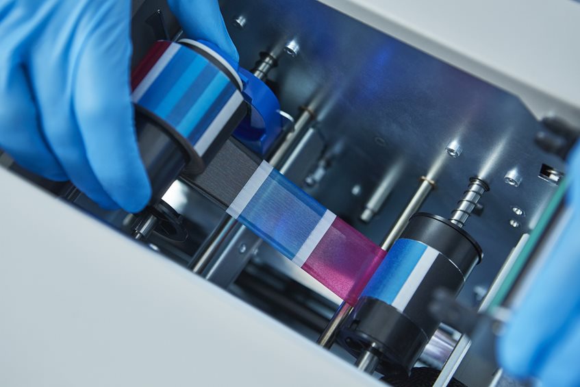 A gloved hand adjusts a color ribbon inside a printer or printing machine.
