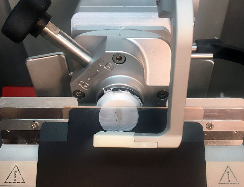 A close-up of a microtome holding a white cylindrical sample, ready for sectioning, with metal levers and adjustment knobs visible.