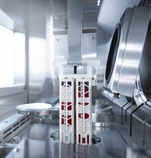 A close-up of automated laboratory equipment processing sample containers inside a sterile, stainless steel environment.