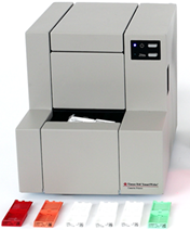 A compact laboratory instrument with buttons and indicator lights, alongside five differently colored plastic slides arranged in front.