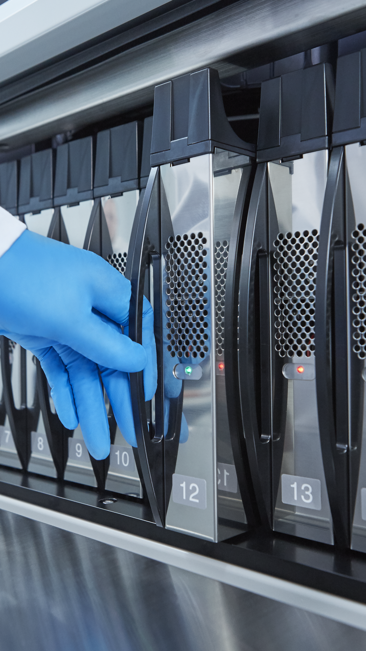 A gloved hand is pulling out a numbered cartridge or tray from a laboratory machine, with indicator lights visible on the device.