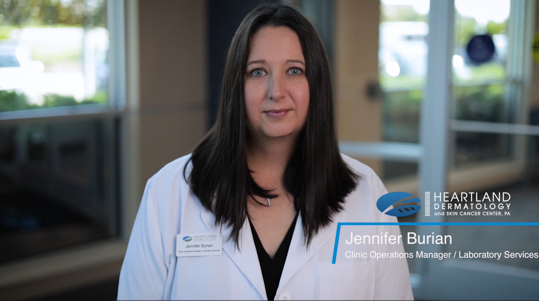 A woman in a white lab coat stands indoors with a name tag reading "Jennifer Burian," identified as Clinic Operations Manager at Heartland Dermatology & Skin Cancer Center, PA.