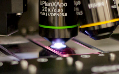 Close-up of a microscope objective lens focusing light on a glass slide during a scientific observation.
