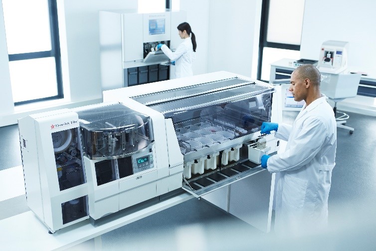 Two scientists in lab coats operate large laboratory analyzers in a bright, modern laboratory setting.