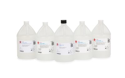 Five clear plastic gallon bottles of laboratory reagent solution are arranged in a row, each with a white label containing text and barcodes.