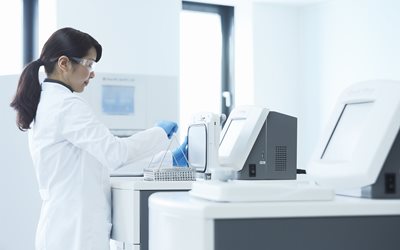 A scientist in a lab coat works with laboratory equipment and test tubes in a bright, modern laboratory setting.