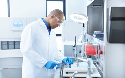 A scientist wearing safety glasses and gloves works with lab equipment at a laboratory workstation.