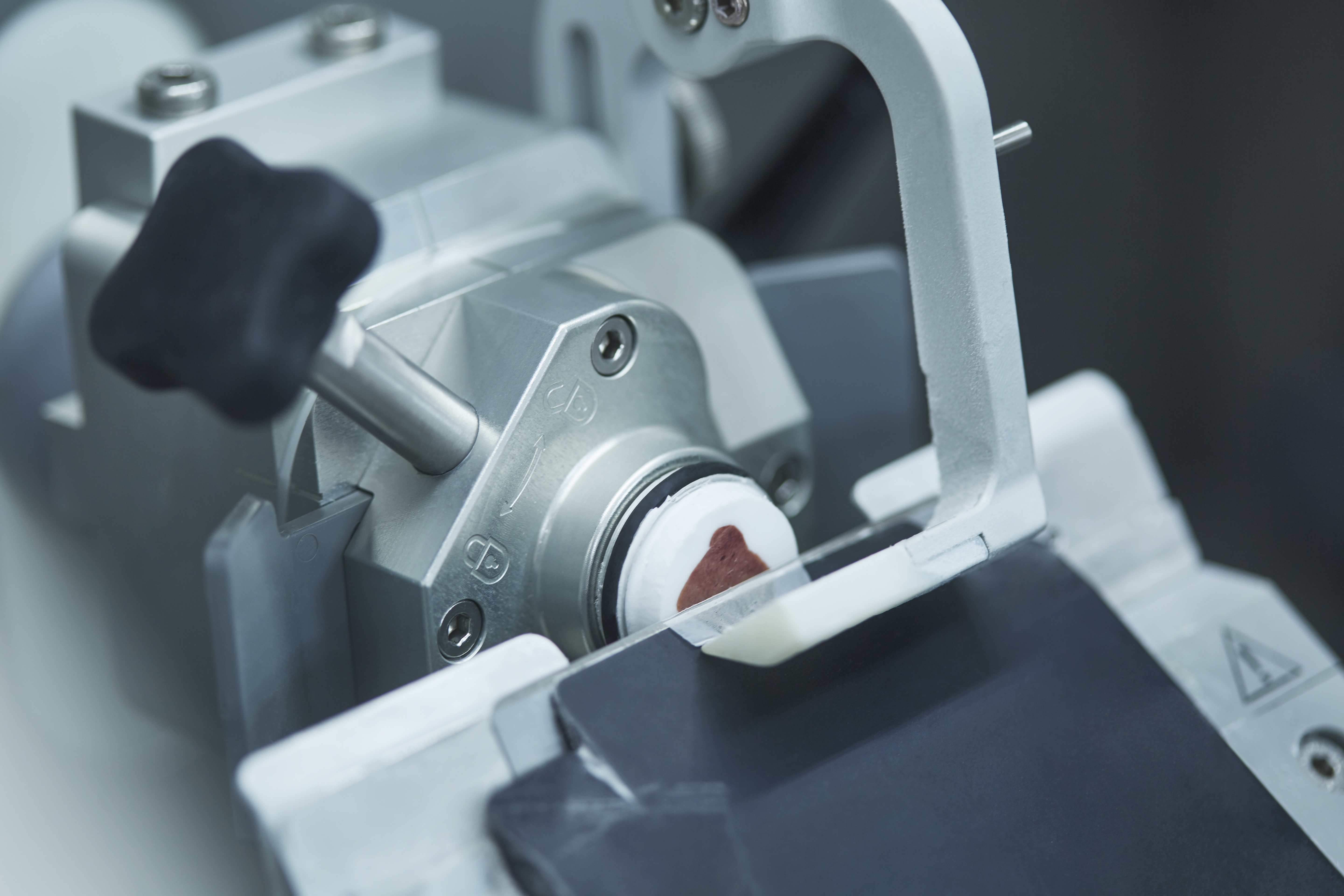 A microtome machine slicing a thin section from a paraffin-embedded biological tissue sample for microscopic examination.