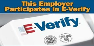 Sign stating "This Employer Participates in E-Verify" with the E-Verify logo and seals for the Department of Homeland Security and Social Security Administration.