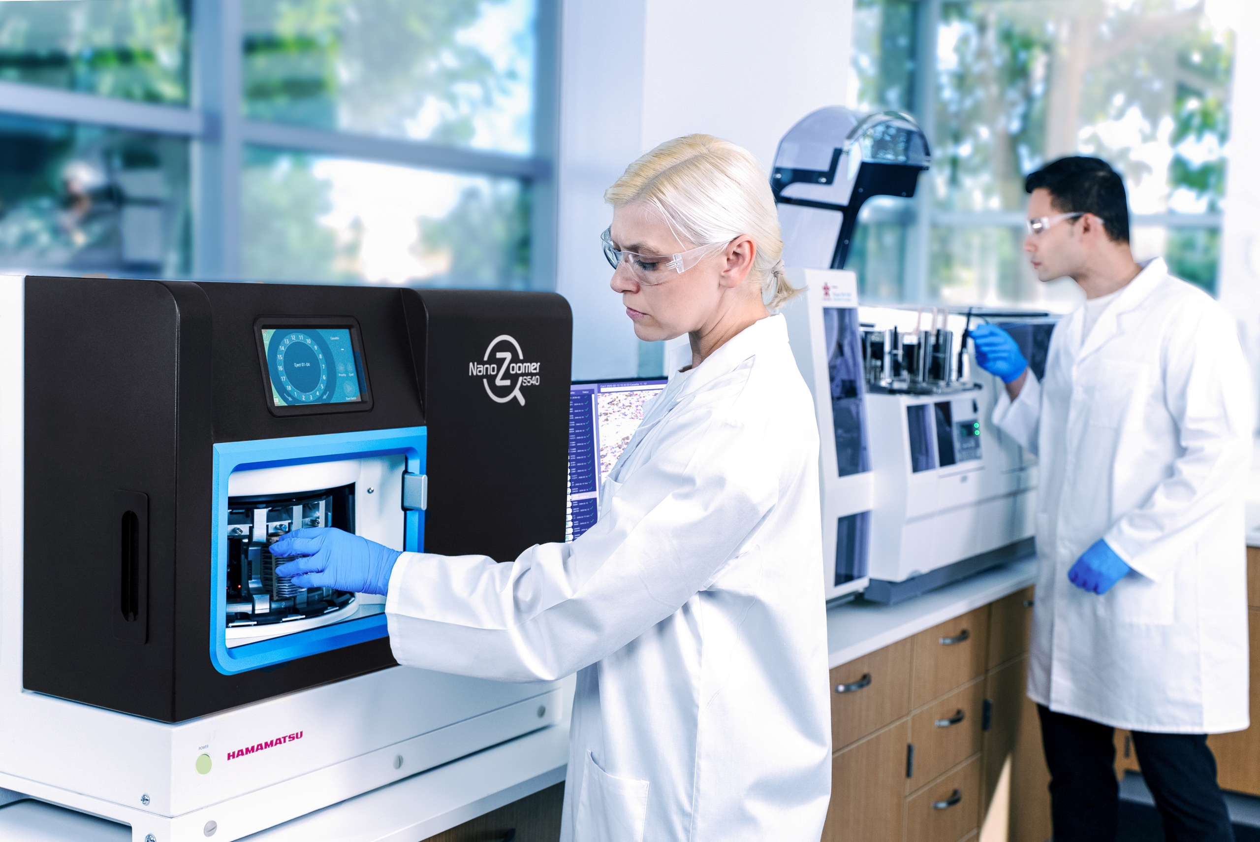 Two scientists in lab coats and gloves work with laboratory equipment in a modern, well-lit laboratory setting.