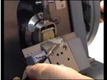 A close-up of hands operating a key cutting machine, with a blank key being cut and shavings visible on the device.